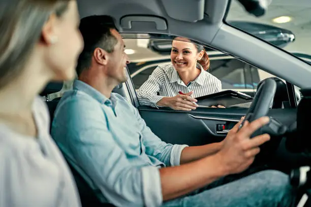 Young female consultant and couple buyers sitting in new car signing contract in auto show. Concept for car rental.