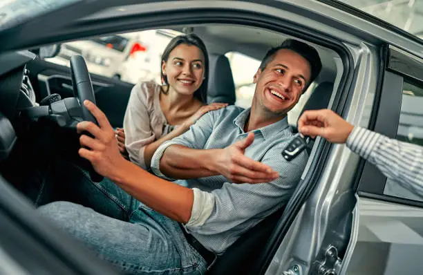 Beautiful happy couple bought a car in the dealership and receives the keys from the manager.