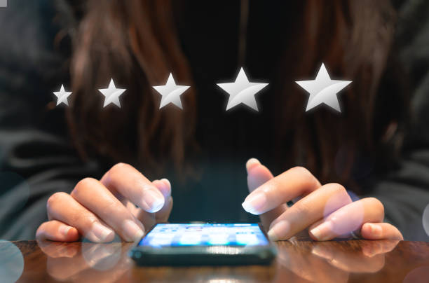 Hands of young woman completing customer satisfaction survey on electronic mobile smartphone with five silver graphic stars stock photo
