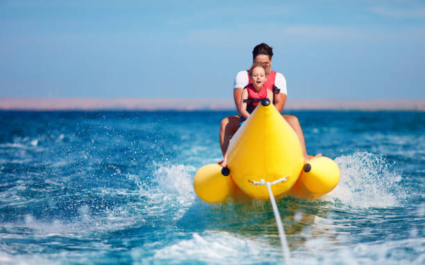 happy family, delighted father and son having fun, riding on banana boat during summer vacation - inflatable raft nautical vessel sea inflatable imagens e fotografias de stock