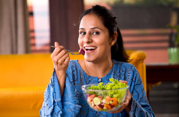 Woman eating fruit salad Happy Indian woman eating fruit salad at home healthy indian food stock pictures, royalty-free photos & images