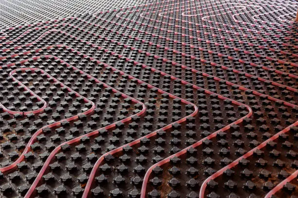 Photo of Underfloor heating system installation. Close up on water floor heating system interior of a new residential building. Pipes filled with propylene glycol. Individual Heating.