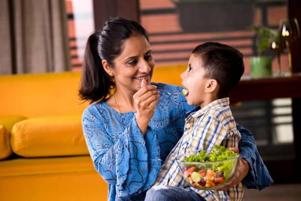 Happy mother feeding fruit salad to son