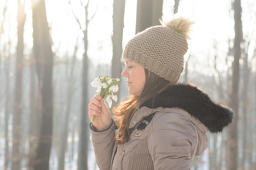 Woman enjoying in fresh snowdrop bouquet in natural parkland. Winter joy.