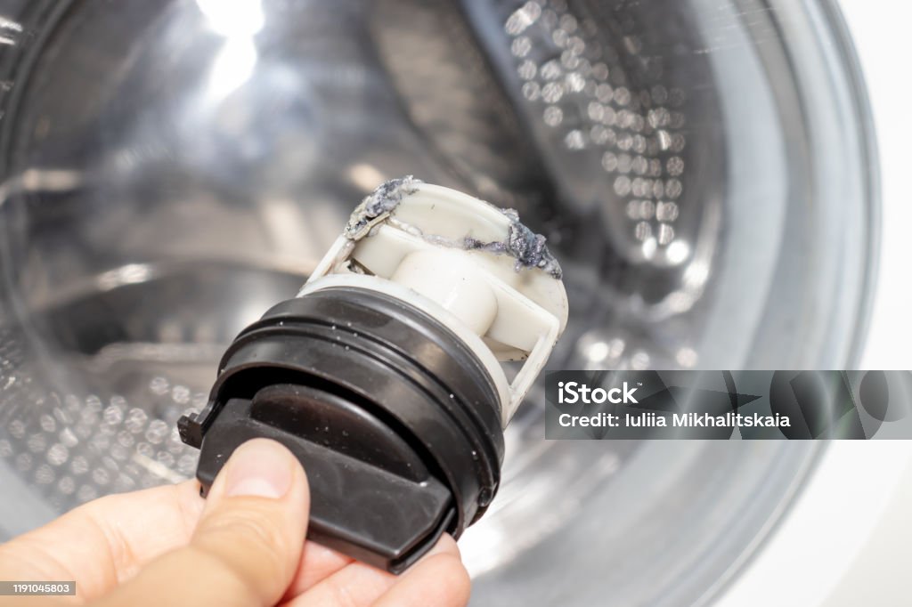 Inspecting washing machine's dirty clogged drain pump filter close up, clean and repair Inspecting washing machine's dirty clogged drain pump filter close up, clean and repair. Washing Machine Stock Photo