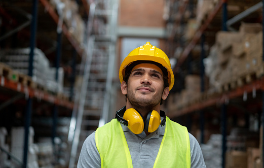 Portrait of a thoughtful worker working at a warehouse wearing a helmet and looking up