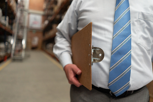 Close-up on a manager working at a warehouse and carrying a clipboard