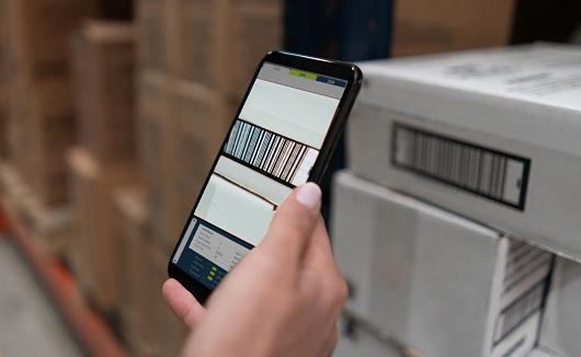 Close-up on a woman scanning products at a warehouse using a cell phone