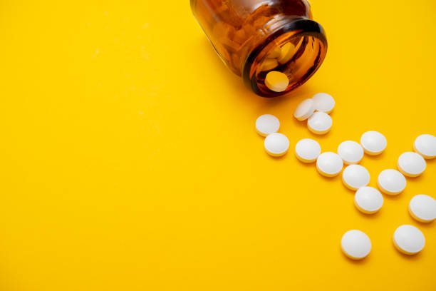 istock Many white tablets and brown glass container close up on yellow background with copy space, autumn and winter viral disease , infection 1191047283
