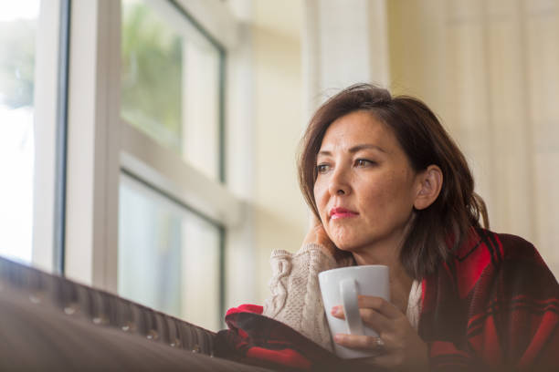 Mature woman looking out the window feeling sad.