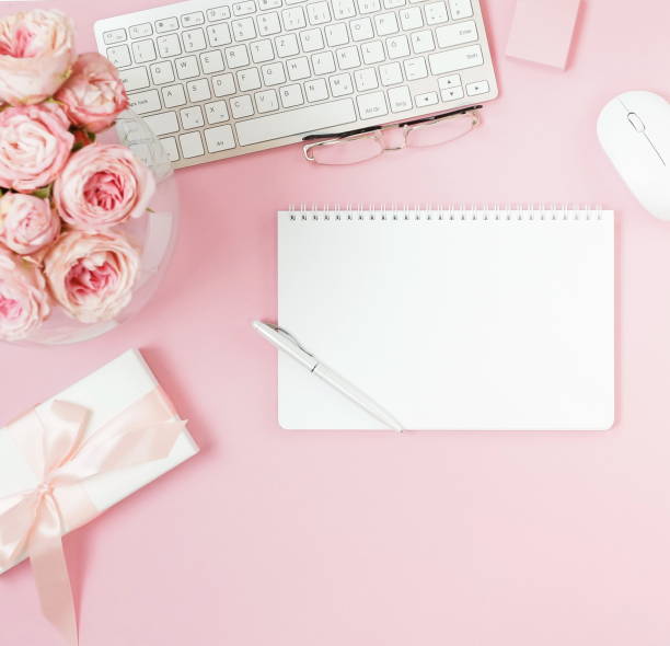 istock flat lay top view women's office desk on  pink background selective focus. Female workspace with laptop, beautiful pink roses flowers in a vase, gift box, accessories, notebooks, glasses. copy space 1191062687