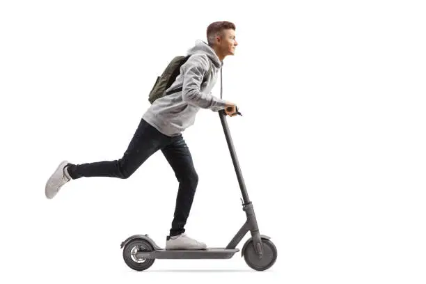 Full length shot of a male student with a backpack riding an electric scooter isolated on white background
