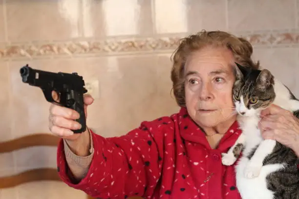 Angry senior woman protecting her cat with a gun.