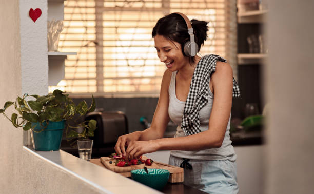 The perfect ingredients for an awesome day Shot of a young woman making a healthy snack with strawberries and listening to music at home chopping food photos stock pictures, royalty-free photos & images