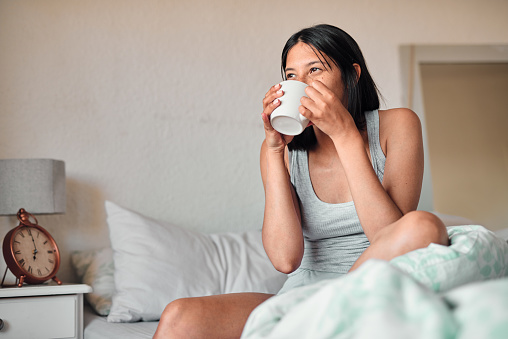 Shot of a young woman enjoying a relaxing cup of coffee in bed at home