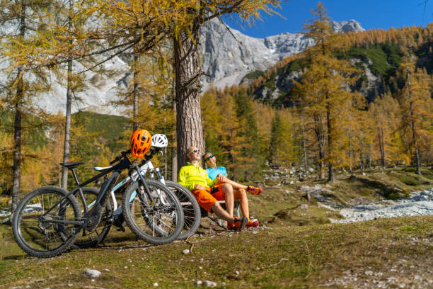 couples de vélo de montagne au repos court sous l'arbre de mélèze le jour ensoleillé d'automne dans les montagnes - larch tree photos et images de collection