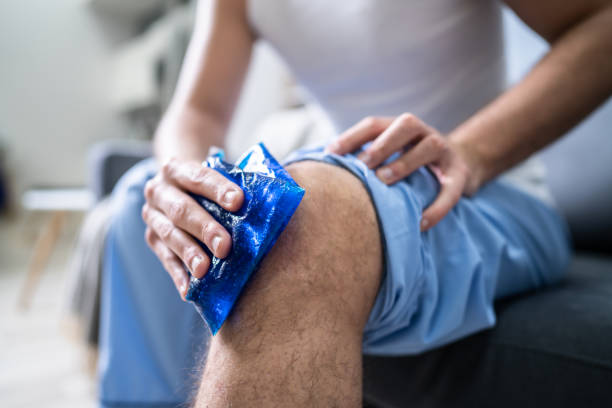 man applying ice gel pack on his knee - ice pack fotos imagens e fotografias de stock