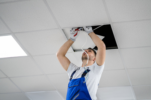 Electrician On Stepladder Installs Lighting To The Ceiling