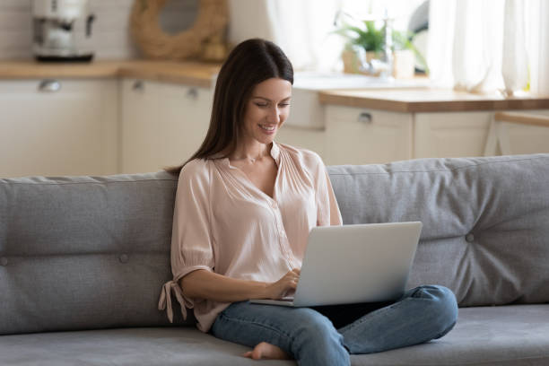 istock Happy beautiful woman using laptop relaxing with technology on couch 1191083749