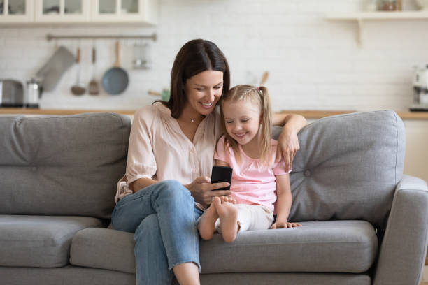 istock Happy mommy and kid daughter enjoying using smartphone on couch 1191083750