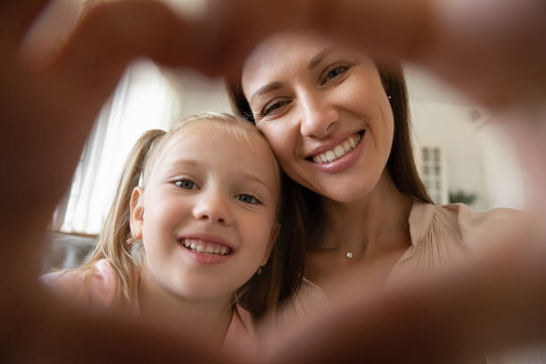 istock Mom and child daughter making heart shape looking at camera 1191083765
