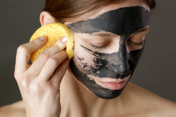 maschera facciale a carbone o fango di argilla nera. bella donna che si toglie la maschera nera dal viso, primo colpo alla testa dello studio. concetto cosmetico naturale. - mud wellbeing spa treatment beautician foto e immagini stock