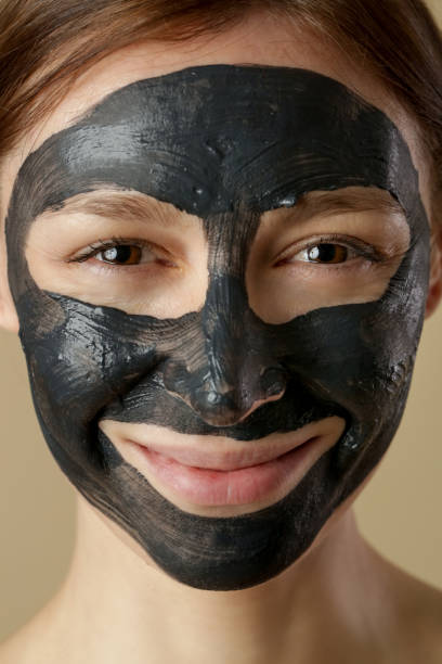 máscara facial de carbón o barro de arcilla negra. hermosa mujer con máscara negra en la cara, tiro de cabeza de estudio de cerca. concepto cosmético natural. - mud wellbeing spa treatment beautician fotografías e imágenes de stock