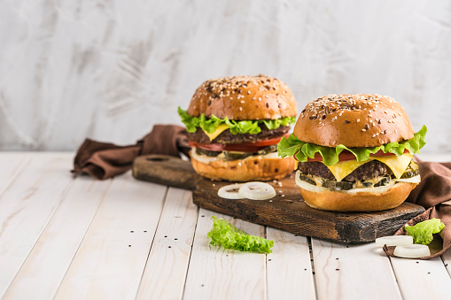 Classic Burger with beef Patty, fresh lettuce, onions, pickles, cheddar cheese and tomatoes on a wooden Board close-up with copyspace. Light background. Fast food. Take away.