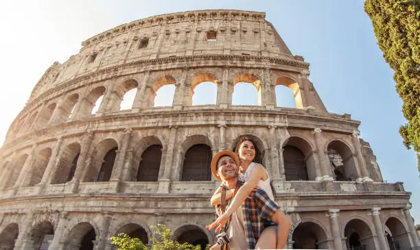 Photo of Young happy couple having fun at Colosseum, Rome. Piggyback posing for pictures.