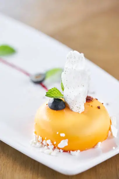 Yellow mousse-cake. French dessert, blueberry, mint and a piece of meringue on a white plate. Stylishly decorated.