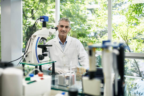 istock Smiling Mature Male Pathologist Sitting at Microscope in Lab 1191113977