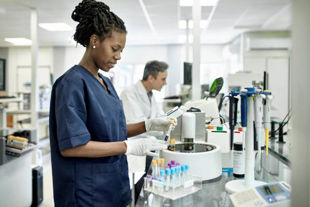 Young African Female Pathology Technician Working in Lab Smiling African female pathology technician in blue scrubs preparing test tubes for analysis in Buenos Aires clinical analysis laboratory. human centrifuge stock pictures, royalty-free photos & images