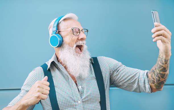 glücklicher senior mann macht selfie beim hören von musik mit kopfhörern - hipster reifen männlichen spaß mit mobilen smartphone playlist-apps - technologie und ältere lifestyle-menschen konzept - headphones music mobile phone tattoo stock-fotos und bilder