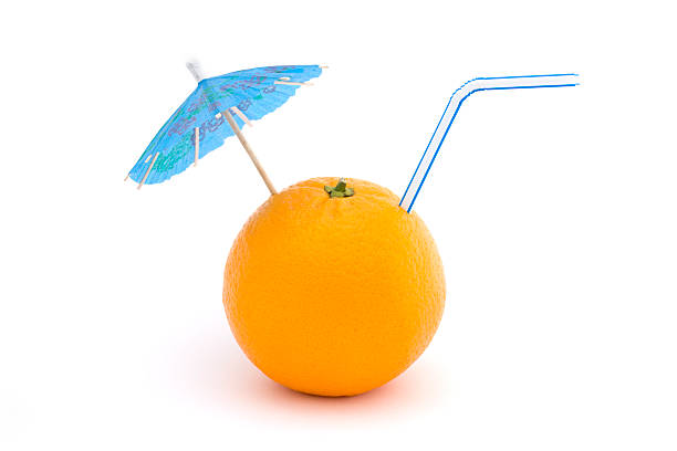 Citrus juice decorated with orange fruit slice, orange peel,paper umbrella and plastic straw isolated on beige paper background. Selective focus.