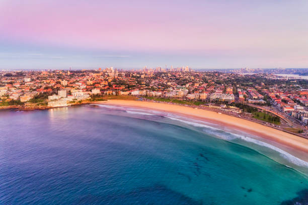 D Bondi Rise High Pink Smooth waters of Pacific ocean surfing on famous Sydney Bondi beach at sunrise in aerial view towards distant city CBD towers and Sydney harbour bridge behind Eastern Suburbs. bondi junction stock pictures, royalty-free photos & images