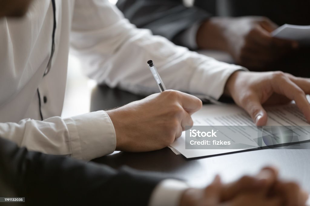 Close up young male manager hands signing contract. Close up young male employee manager customer hands signing paper contract after checking. Millennial investor client put signature at business agreement between partners. Editor making corrections. Business Stock Photo