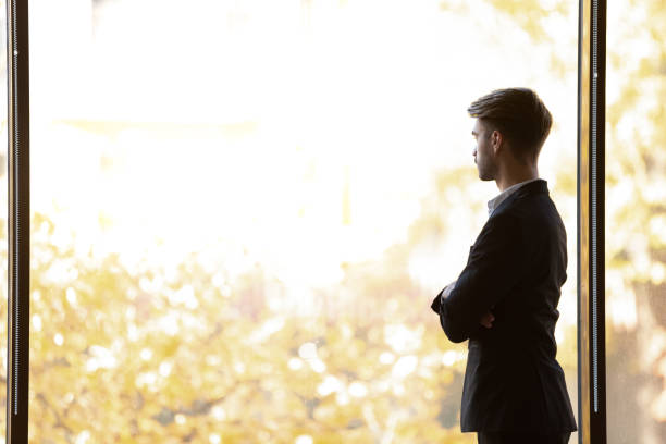 Concentrated thoughtful young businessman looking away at panoramic office window.