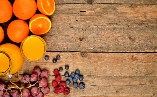 View from above of jug with orange juice, fresh oranges, apples, grapes, raspberries and blueberries on a wooden table - fruit background