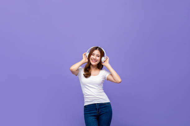 Pretty Asian woman dancing and listening to music on headphones Young pretty cute Asian woman looking happy and relaxed dancing and listening to streaming music on headphones isolated on purple background free girl download stock pictures, royalty-free photos & images