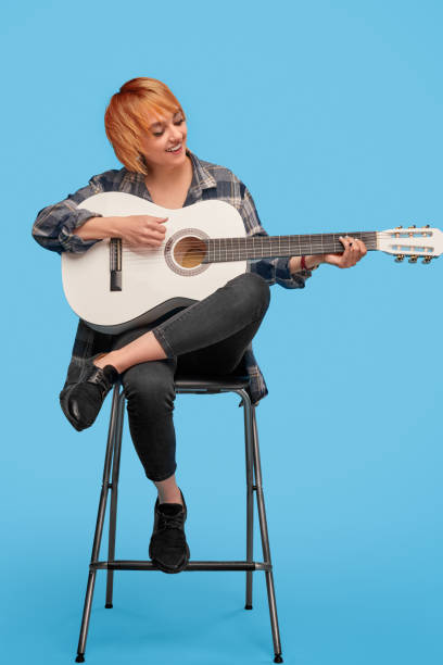 istock Cheerful woman playing guitar on chair 1191133464