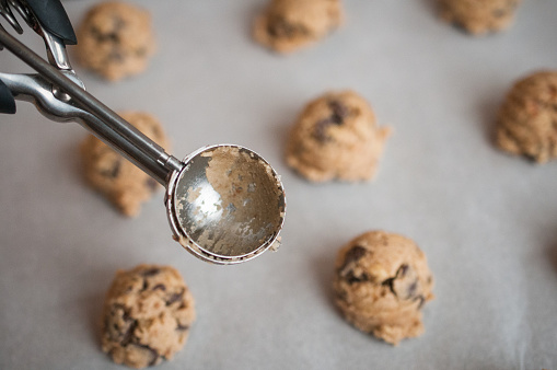 An overhead photograph of a baking pan with raw chocolate chip  cookies dough \nand scoop