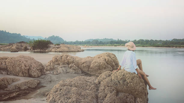 Woman traveler sitting on a rock in sea shore of the Thailand beach. Vintage film grain filter effect styles stock photo