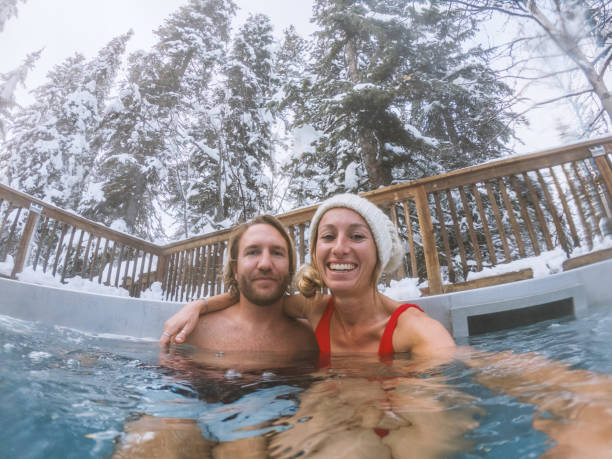 pareja joven tomando selfie en spa jacuzzi en invierno rodeado de nieve joven pareja tomando selfie en spa jacuzzi en invierno rodeado de nieve - swimwear bikini swimming pool red fotografías e imágenes de stock