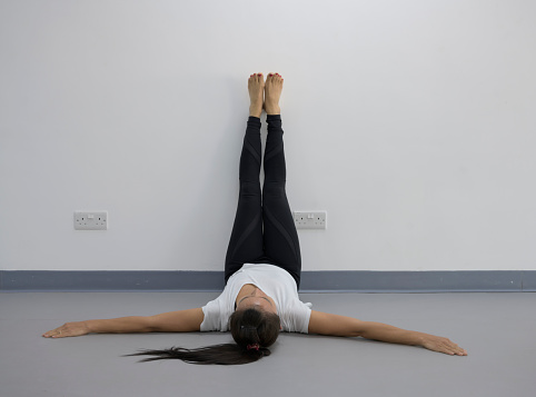 Yoga woman feet up relaxing on wall background