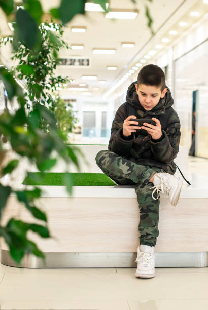 adolescent jouant avec le smartphone dans le centre commercial moderne. concept de technologie et de communication avec l'enfant dans l'intérieur contemporain de bâtiment. - 16711 photos et images de collection