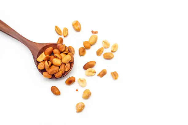 Roasted peanuts in a wooden spoon, isolated on a white background