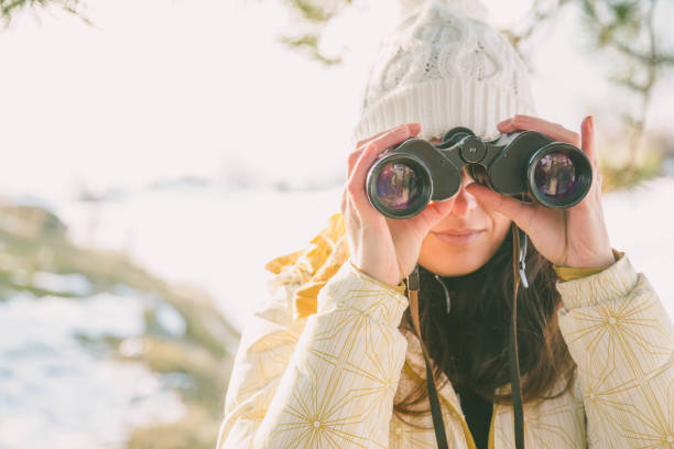 istock The girl in a White cap with a backpack in the winter in a forest looking through binoculars 1191183274