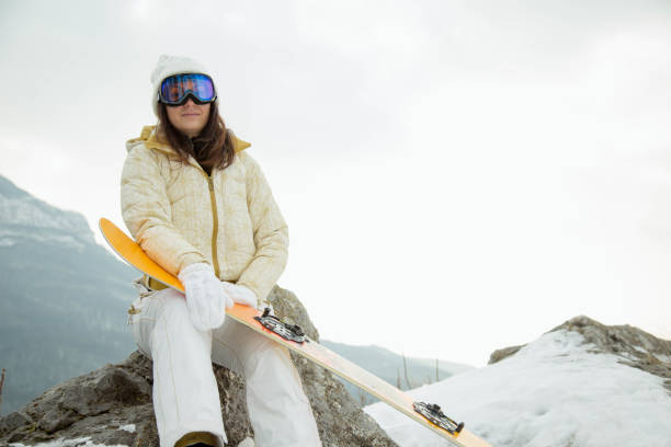 istock Woman holding snowboard with mountains in background 1191183298