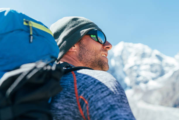 retrato do homem não raspado do caminhante com trouxa e óculos de sol de proteção uv no fundo do pico de taboche 6495m, apreciando vistas da montanha durante a rota de trekking do acampamento baixo de everest. - snow glasses - fotografias e filmes do acervo