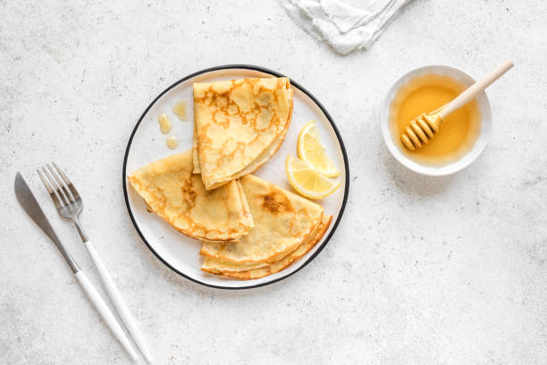 Crepes and Honey Crepes with Lemon and Honey on white background, top view. Homemade thin crepes on plate for breakfast or dessert. blini photos stock pictures, royalty-free photos & images